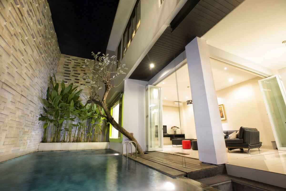 A modern indoor pool area with a glass door leading to a living space.