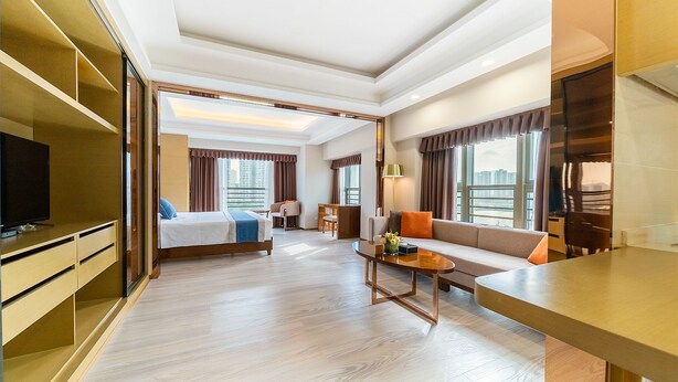 A hotel room with a bed, a sofa, a TV, a desk, and a view of the city. - Zhuhai Boruiwan Binjiang Hotel (Zhuhai)