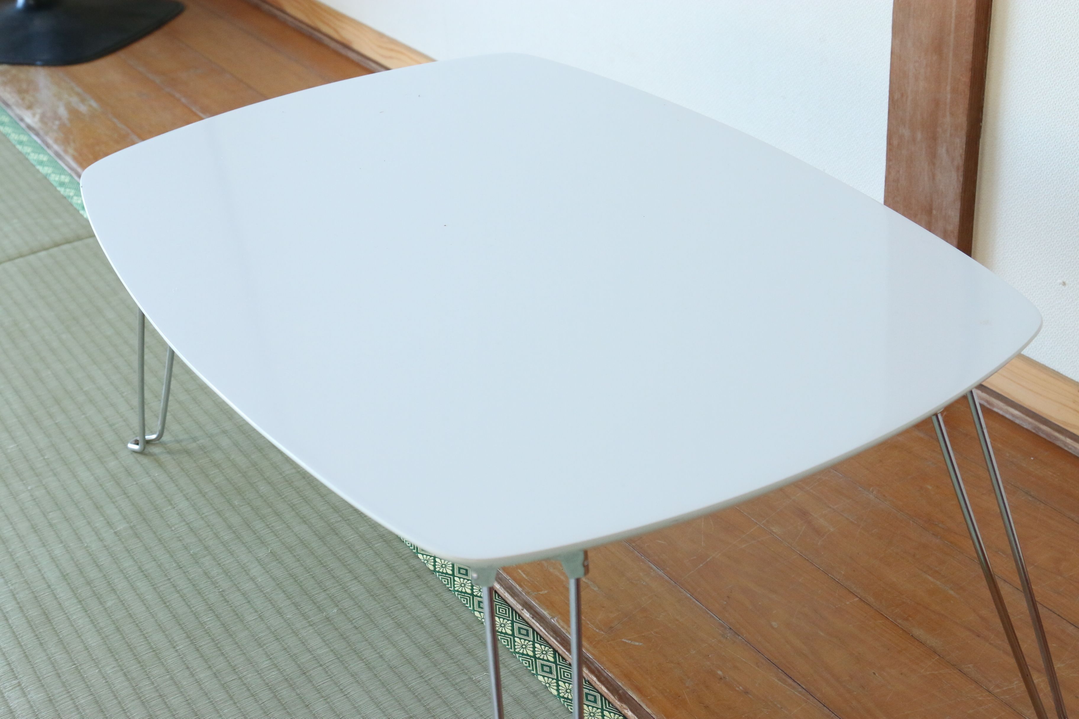 A white chair with metal legs, positioned on a wooden floor next to a white wall.