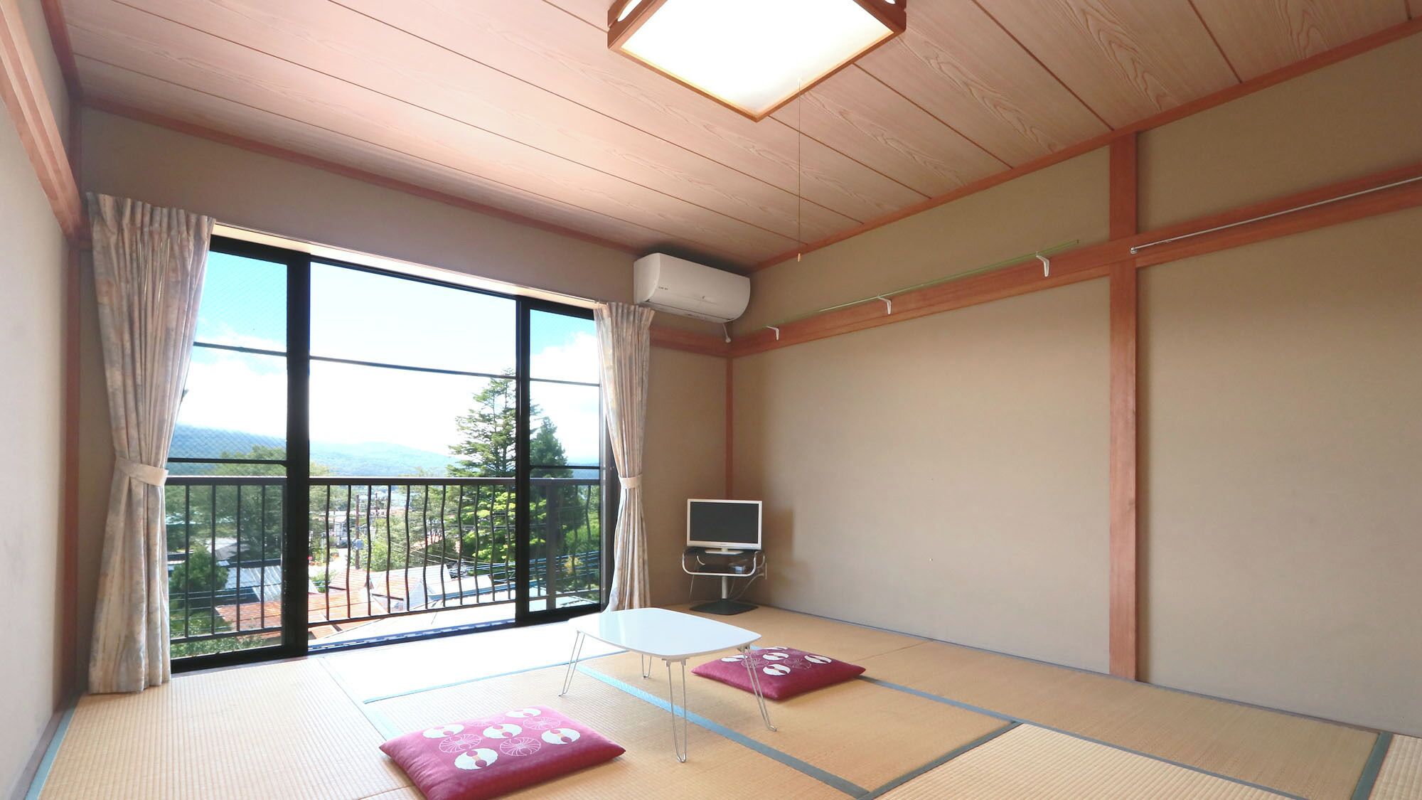 A room with tatami flooring, a TV, a small table, and a view of a balcony with a railing.