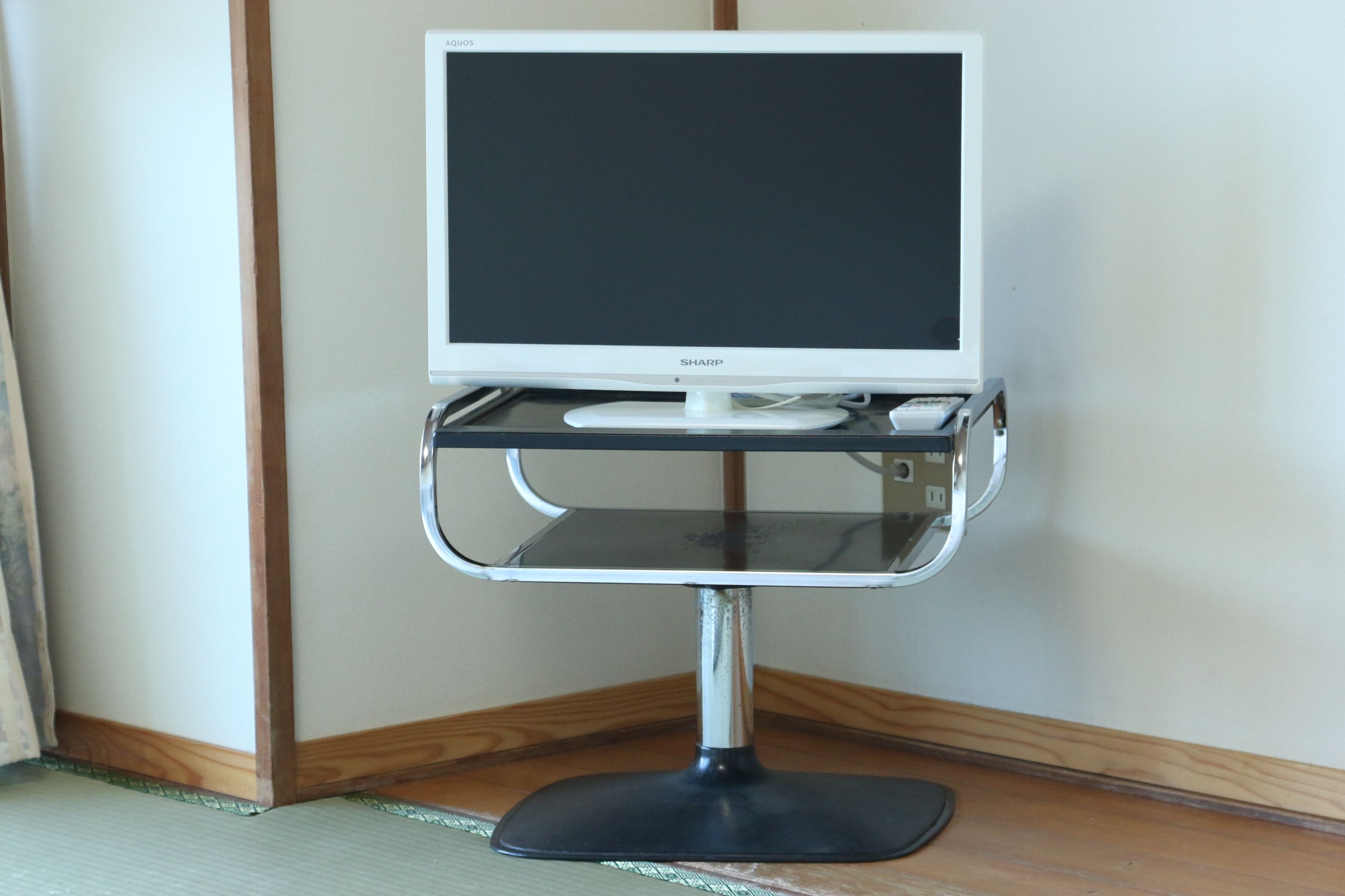 A white Sharp monitor on a chrome stand with a black base, positioned against a plain wall.