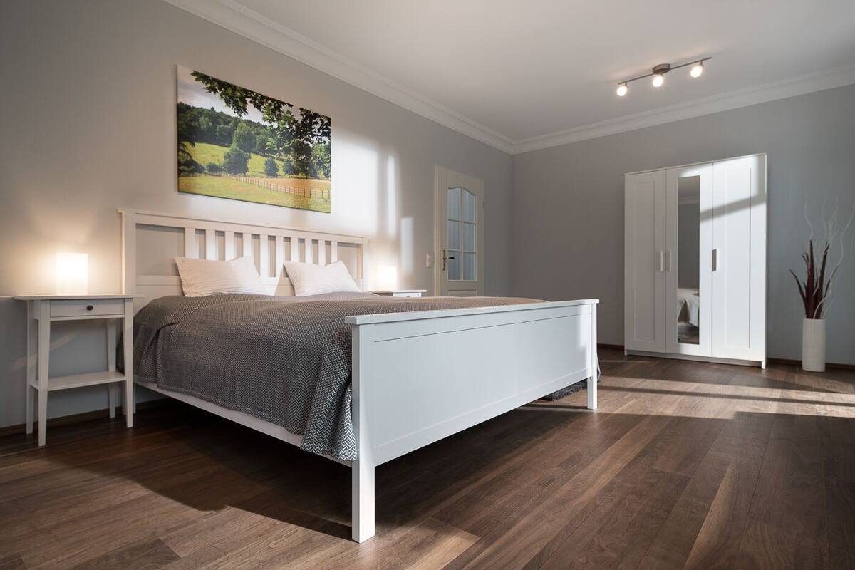 A bedroom with a bed, nightstands, a wardrobe, and a painting on the wall.