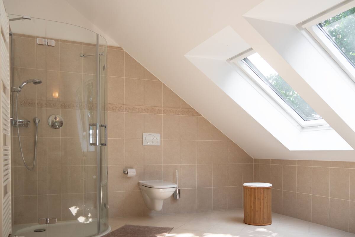 A modern bathroom with a glass shower enclosure, a toilet, and a small wooden stool.