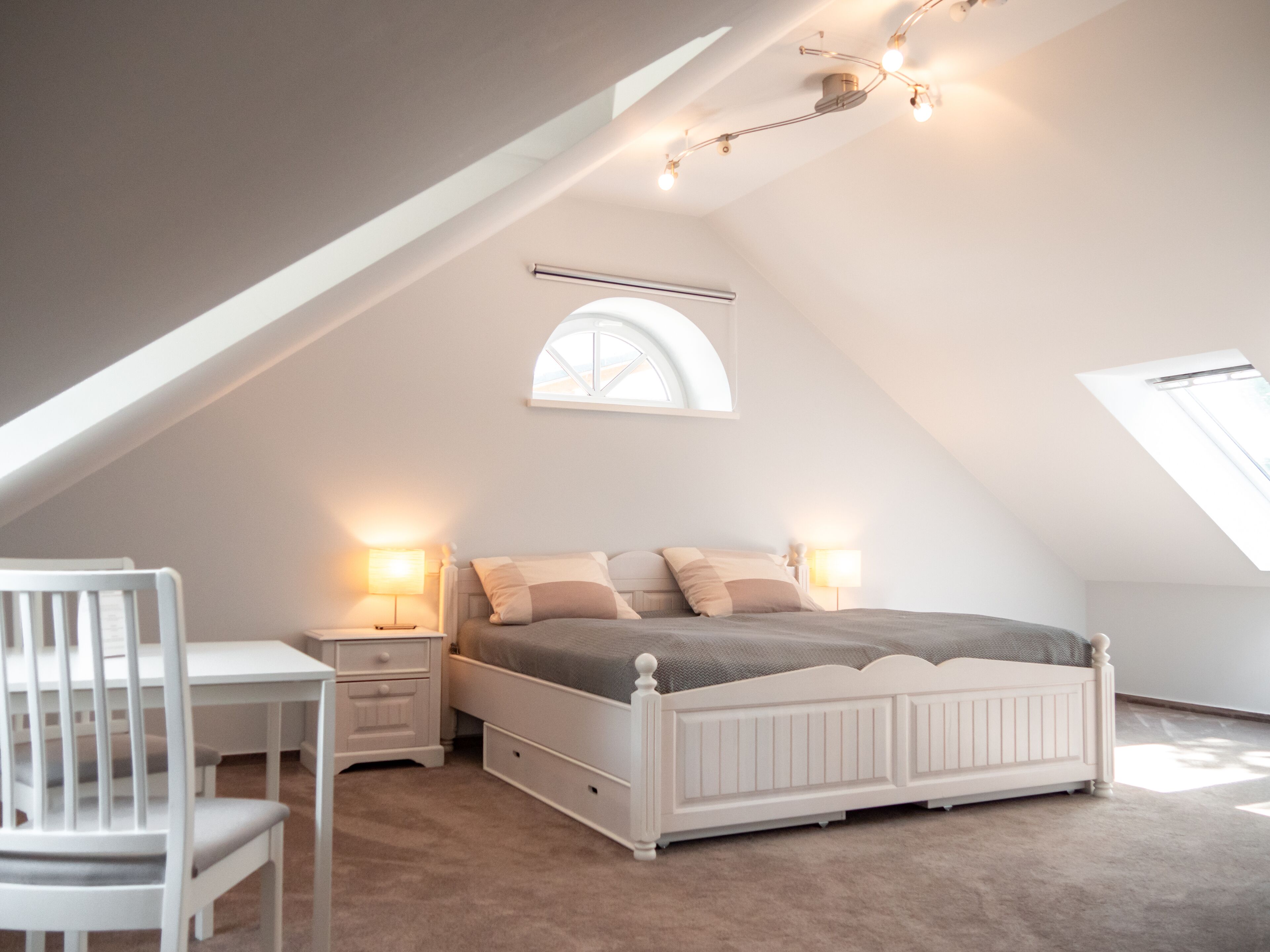 A bedroom with a sloped ceiling, a bed, a desk, and two bedside lamps.