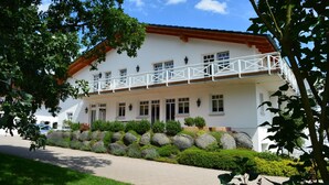 A white building with a balcony, surrounded by a landscaped garden with rocks and shrubs.