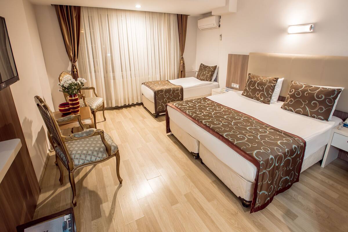 A hotel room with a large bed, a smaller bed, a desk, a chair, and a TV.
