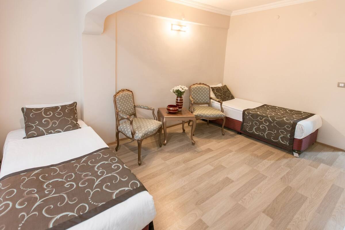 A hotel room with two beds, a small table with chairs, and a vase of flowers.