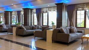 A modern hotel lobby with a seating area featuring sofas and armchairs, large windows with curtains, and a tiled floor. - Bolu Termal Otel (Bolu)
