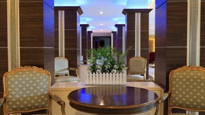 A lobby with a round table and two ornate chairs, a white decorative planter with green plants, and a red chair in the background. - Bolu Termal Otel (Bolu)