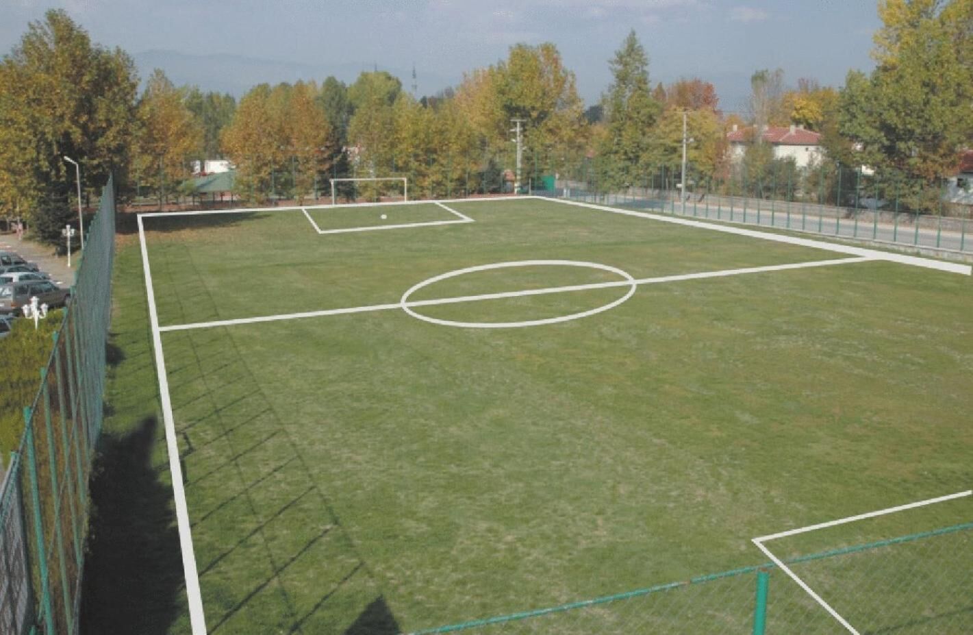 An outdoor soccer field with goalposts and a net, surrounded by a fence and trees.