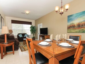 A dining area with a wooden table set for four, a television in the background, and a painting on the wall. - Ov3718 - Windsor Palms Resort - 3 Bed 2 Baths Townhome (Kissimmee)