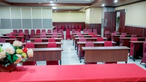 Una sala de conferències amb files de cadires vermelles i escriptoris de fusta, un mantell de taula vermell sobre la taula del davant i un ram de flors.