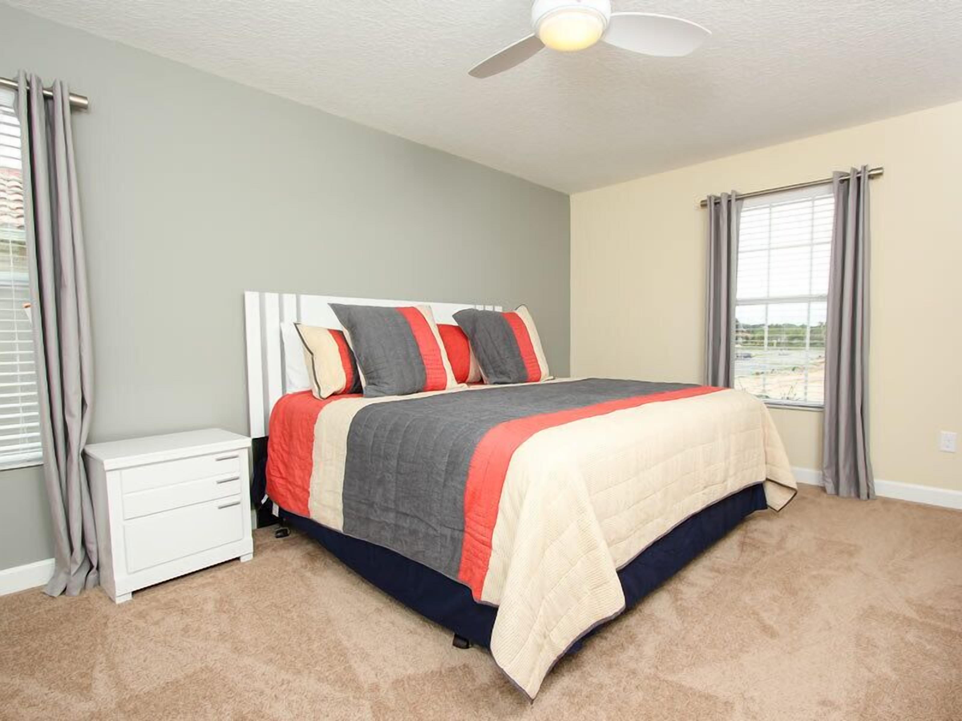 A bedroom with a bed, a nightstand, a ceiling fan, and a window with curtains.