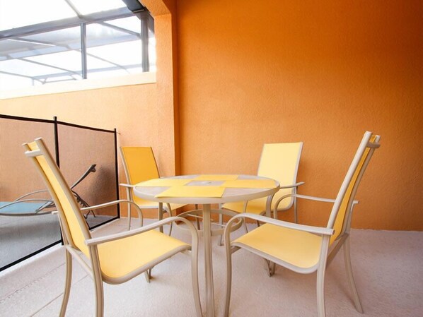 A room with a round table and four chairs, a window with a metal frame, and a plain orange wall. - Ov3708 - Paradise Palms - 4 Bed 3 Baths Townhome (Kissimmee)