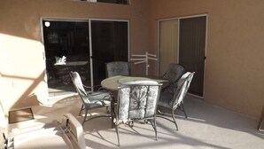 Eine Terrasse mit rundem Tisch und vier Stühlen, eine Glastür und Blick ins Innere.