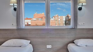 A hotel room with two beds, a large window with a city view, and wall-mounted lamps. - Hostal Golden Alcalá (Madrid)