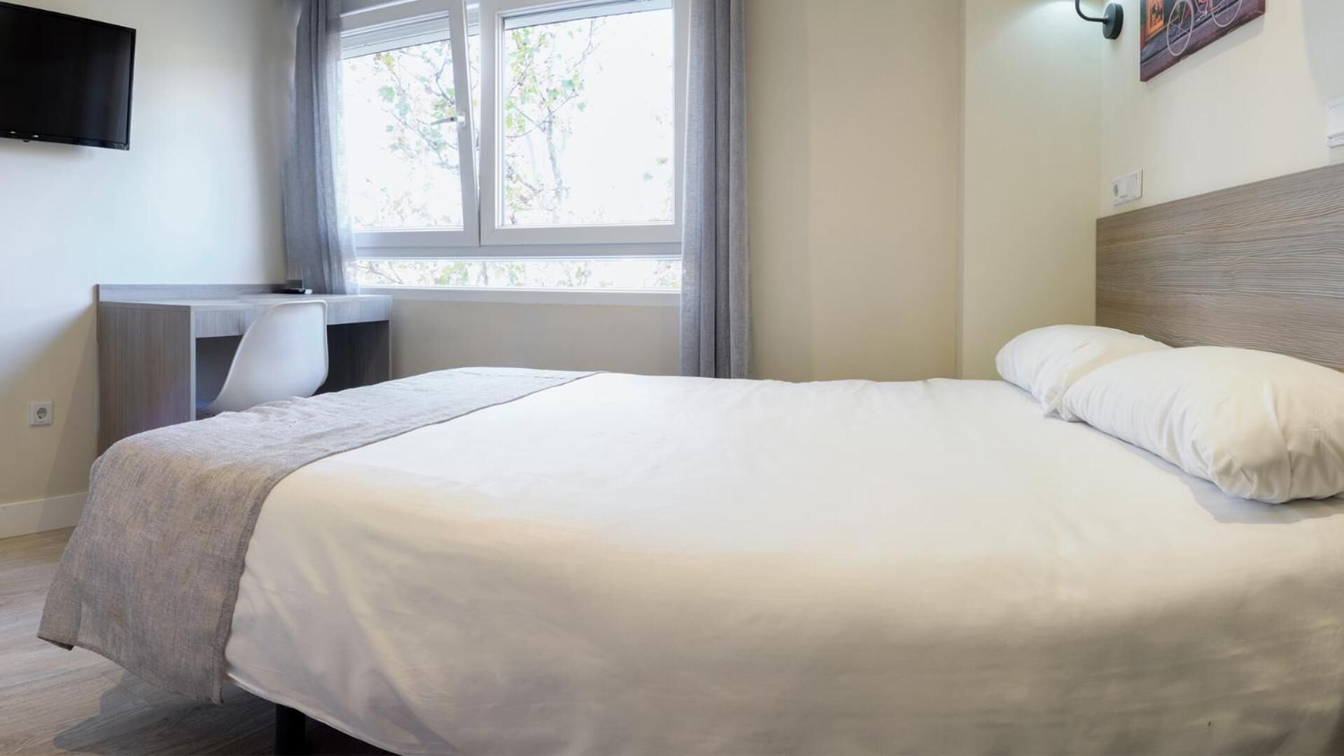 A bedroom with a bed, a desk, and a TV.