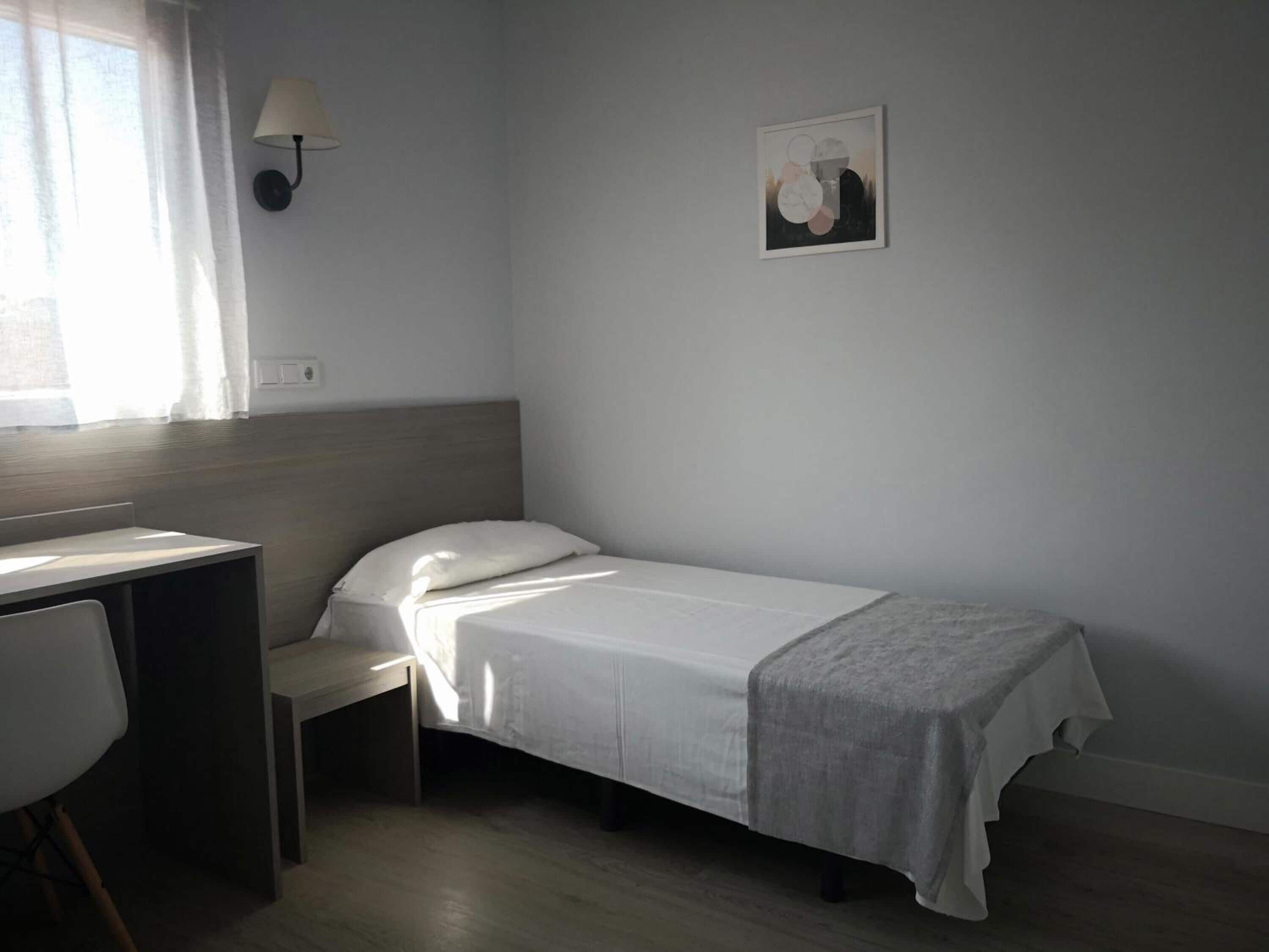 Un dormitorio pequeño y ordenado con una cama individual, un escritorio y una silla.