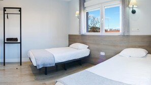 Habitació amb dos llits individuals, un frontal de fusta, una petita prestatgeria i una finestra amb vista a l'exterior.