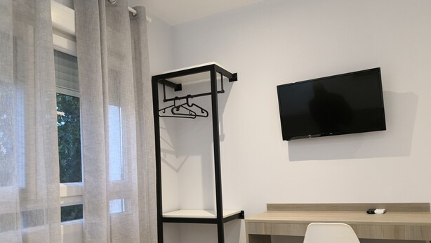 A room with a desk, a chair, a TV mounted on the wall, and a clothing rack. - Hostal Golden Alcalá (Madrid)