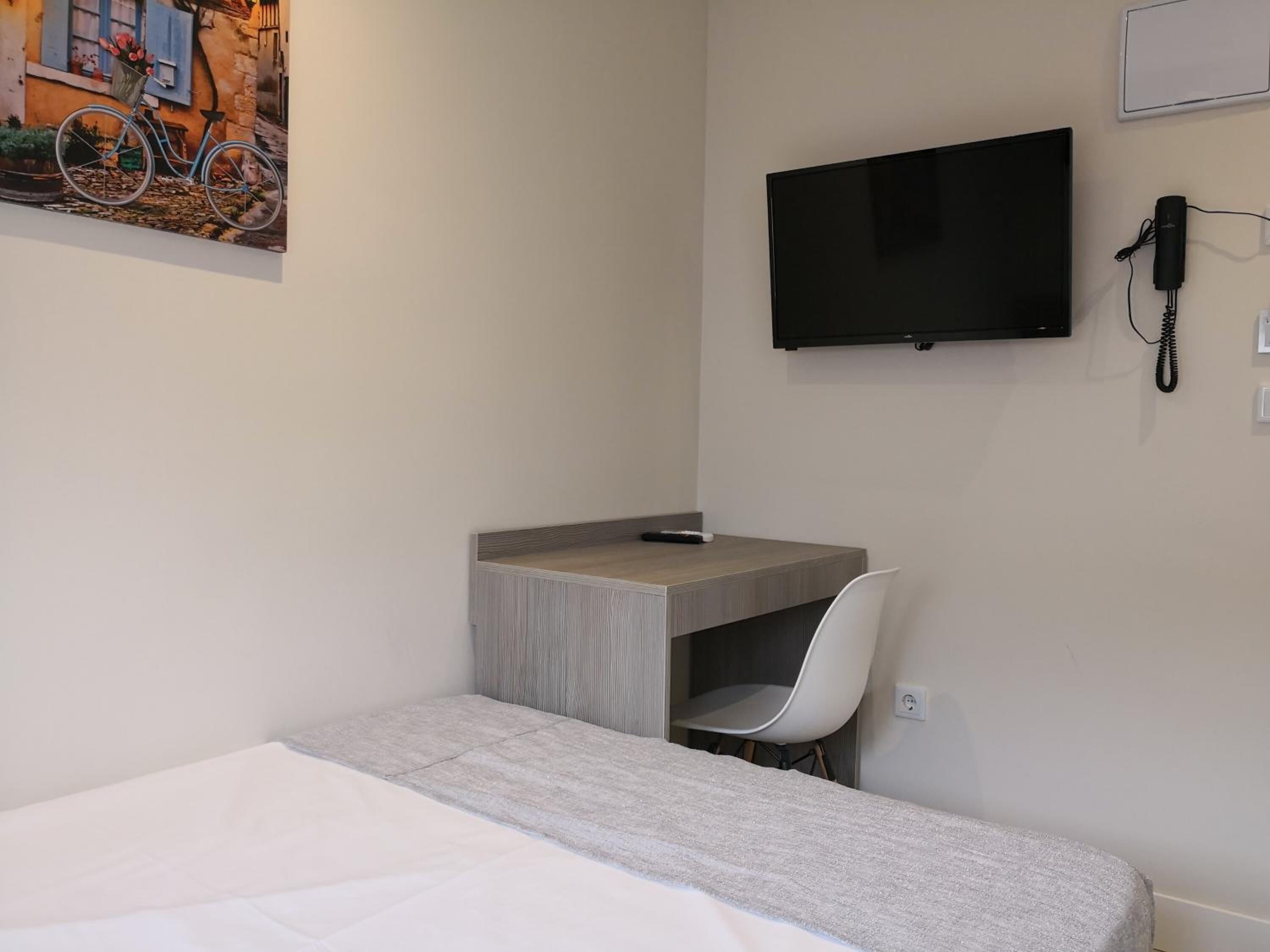 Una habitación de hotel con una cama, un escritorio con una silla, un televisor y un teléfono.
