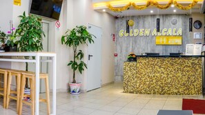 Zona d'arribada amb sòl de rajoles, mostrador de recepció amb un disseny de mosaic i plantes en testos.