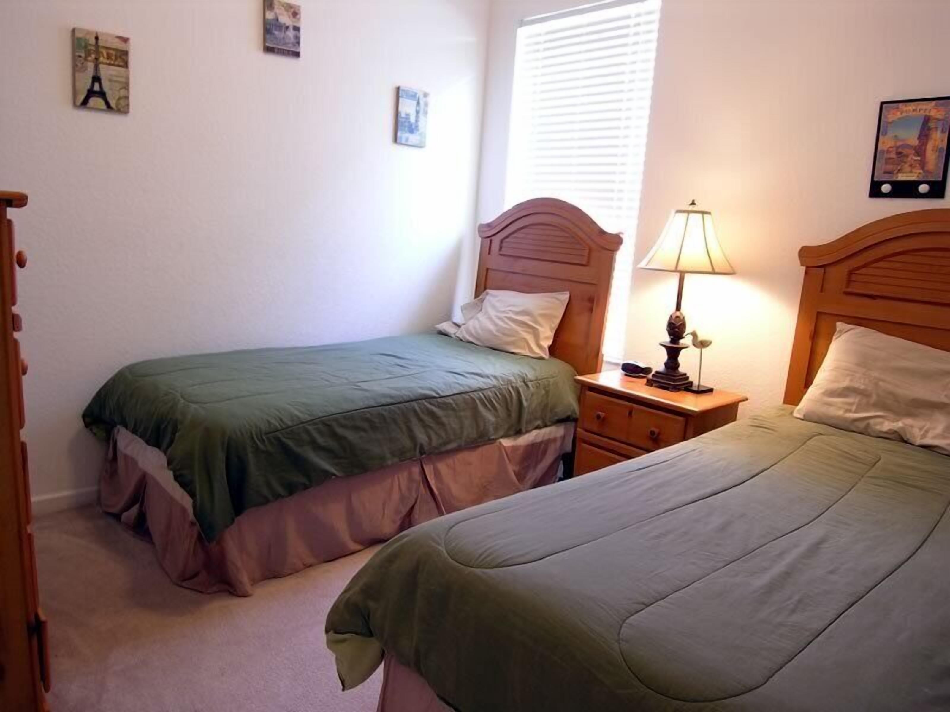 Un dormitorio con dos camas individuales, una mesita de noche con lámpara y un aparador.