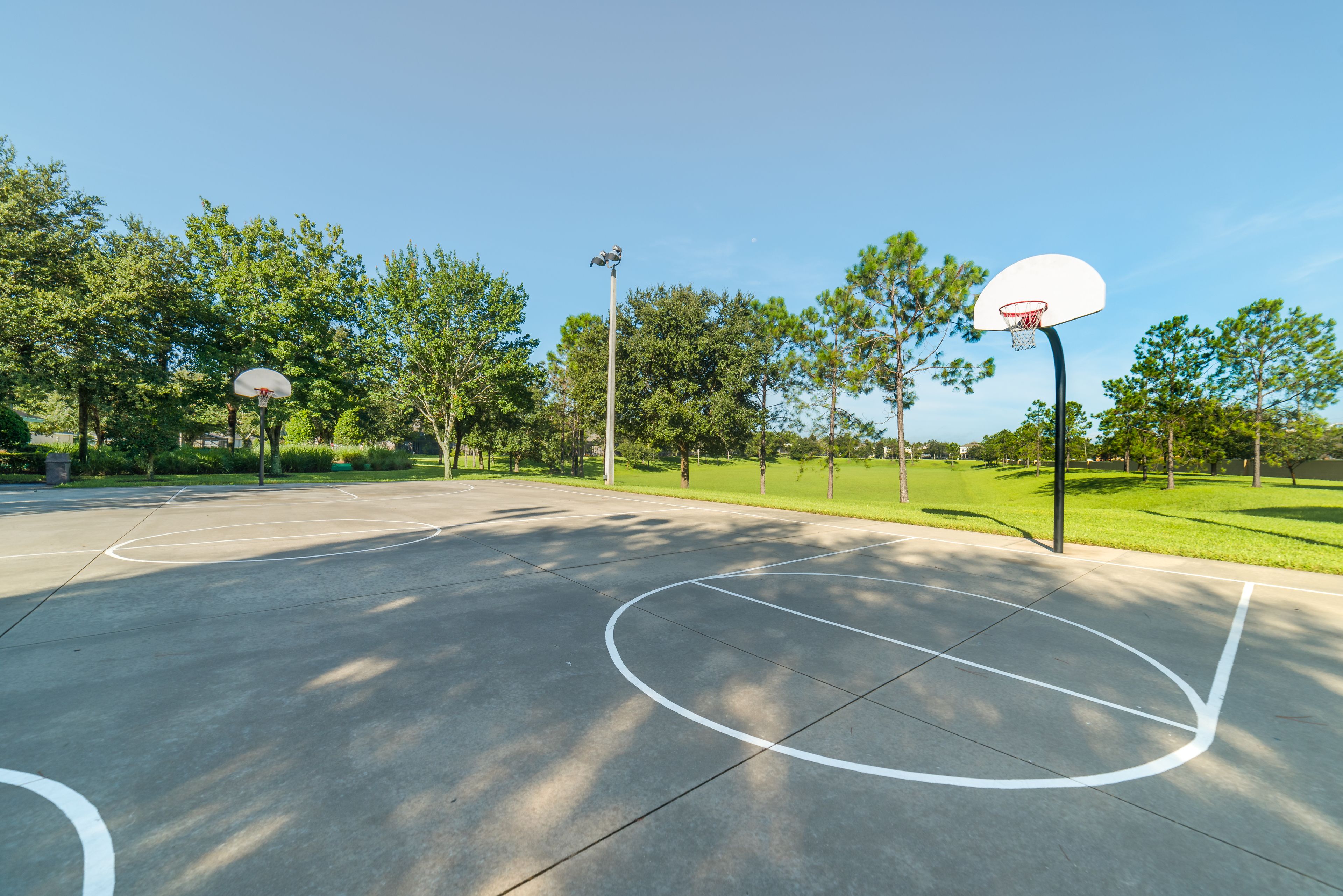 An outdoor basketball court with two hoops, surrounded by trees and grass.