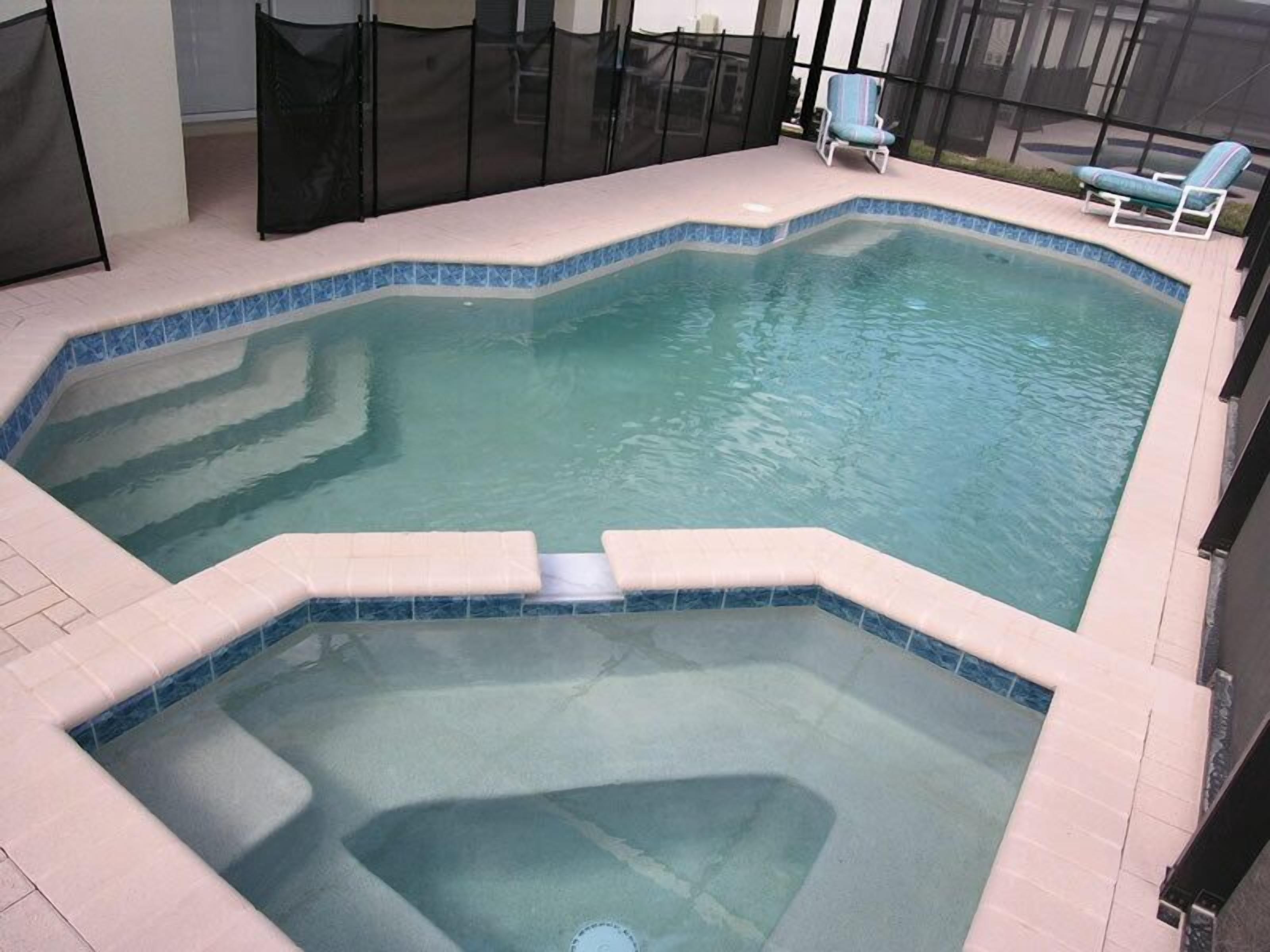 Una piscina interior rectangular con borde de azulejos, un jacuzzi en el centro y dos sillones de descanso junto a la piscina.