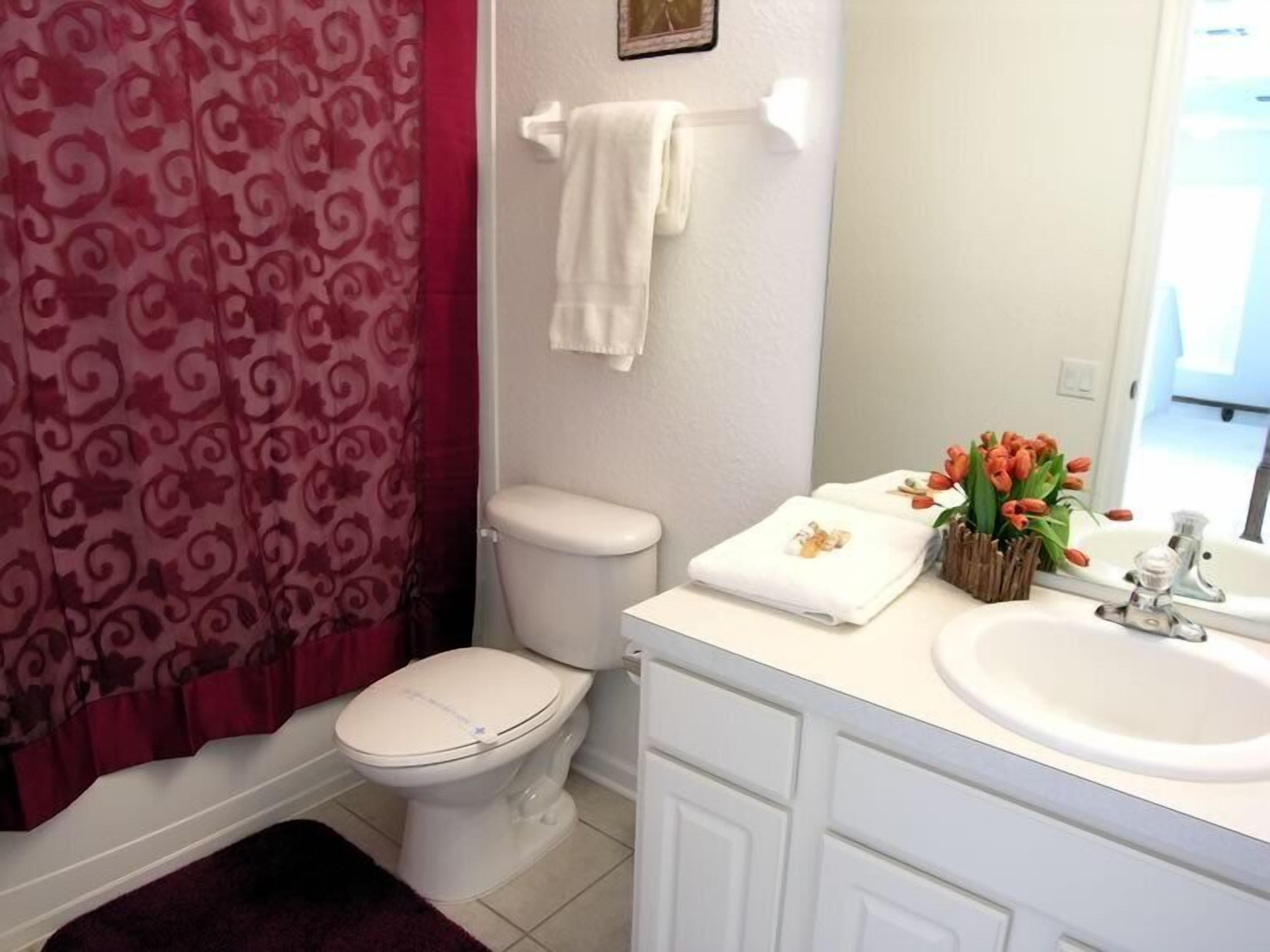 A bathroom with a toilet, a sink, and a mirror. There is a towel rack with a white towel and a vase with flowers.