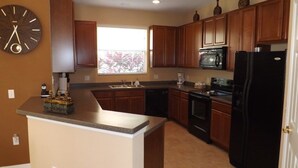 A kitchen with wooden cabinets, a black refrigerator, a microwave, and a clock on the wall. - Ov3688 - Compass Bay - 4 Bed 2.5 Baths Townhome (Kissimmee)