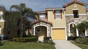 A two-story residential building with a stone facade, a yellow garage door, and a small porch with a stone archway. - Ov3688 - Compass Bay - 4 Bed 2.5 Baths Townhome (Kissimmee)