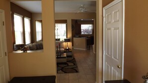 A hallway leading to a living room with a sofa, a coffee table, and a lamp. There is a door on the right and a window on the left. - Ov3688 - Compass Bay - 4 Bed 2.5 Baths Townhome (Kissimmee)