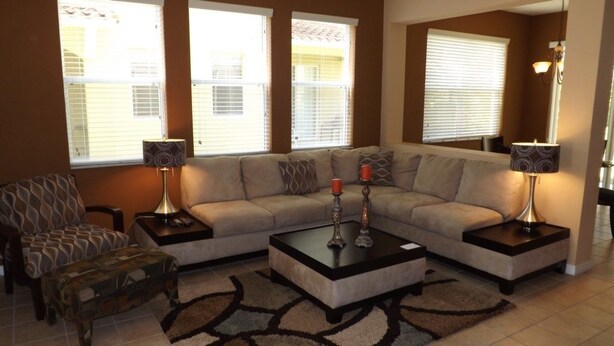 A living room with a sectional sofa, two side tables with lamps, a patterned ottoman, and a coffee table. - Ov3688 - Compass Bay - 4 Bed 2.5 Baths Townhome (Kissimmee)