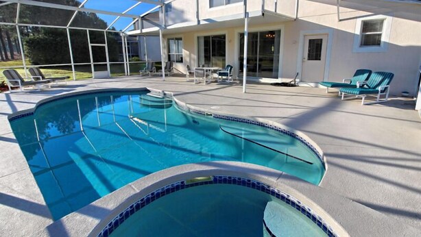 A swimming pool with a covered patio area, lounge chairs, and a house in the background.