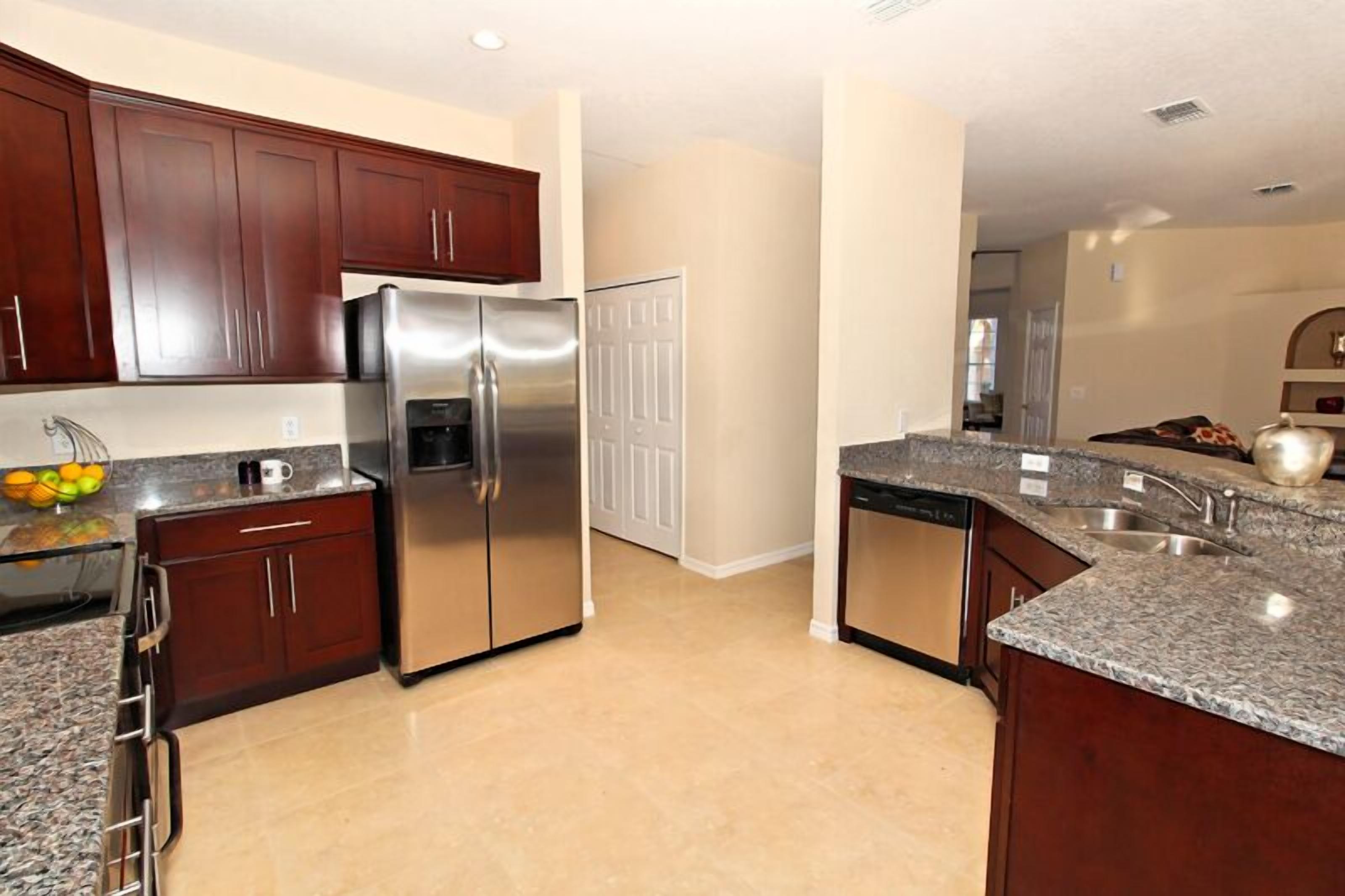A modern kitchen with dark wood cabinets, stainless steel appliances, granite countertops, and a tiled floor.