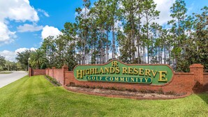 A sign for Highlands Reserve Golf Community with a brick wall and grass in front.