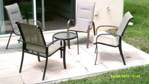 Eine Terrasse im Freien mit vier Stühlen und einem kleinen runden Tisch.