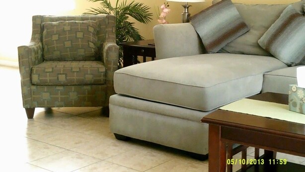 Ein Wohnzimmer mit einem gemusterten Sessel, einem grauen Sofa, einem kleinen Tisch und einer Lampe.