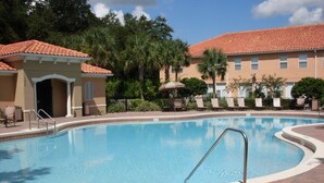 Ein Swimmingpool mit Fliesen umgeben, Liegestühle und ein Gebäude mit rotem Ziegeldach.