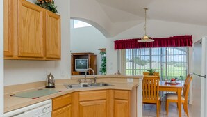 A kitchen with wooden cabinets, a built-in oven, a sink, and a dining area with wooden chairs and a table. - Ovm3553 - Emerald Island - 5 Bed 3 Baths Villa (Kissimmee)