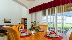 A dining area with a wooden table set for four, surrounded by chairs. A red curtain and a window with vertical blinds are visible. - Ovm3553 - Emerald Island - 5 Bed 3 Baths Villa (Kissimmee)