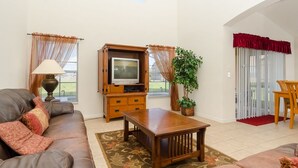 A living room with a leather sofa, wooden TV stand, and a dining area with a chair and table. - Ovm3553 - Emerald Island - 5 Bed 3 Baths Villa (Kissimmee)