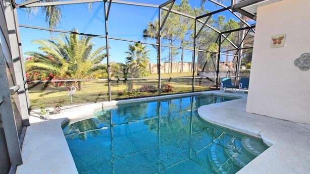 Uma piscina com vista clara para palmeiras e uma área gramada ao fundo.
