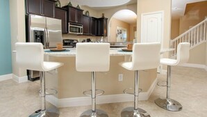 A modern kitchen with dark cabinets, stainless steel appliances, and a central island with bar stools. - Ov3520 - Solterra Resort - 5 Bed 4.5 Baths Villa (Davenport)
