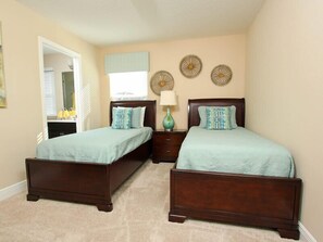 Un dormitorio con dos camas individuales, una mesita de noche con lámpara y decoración en la pared.