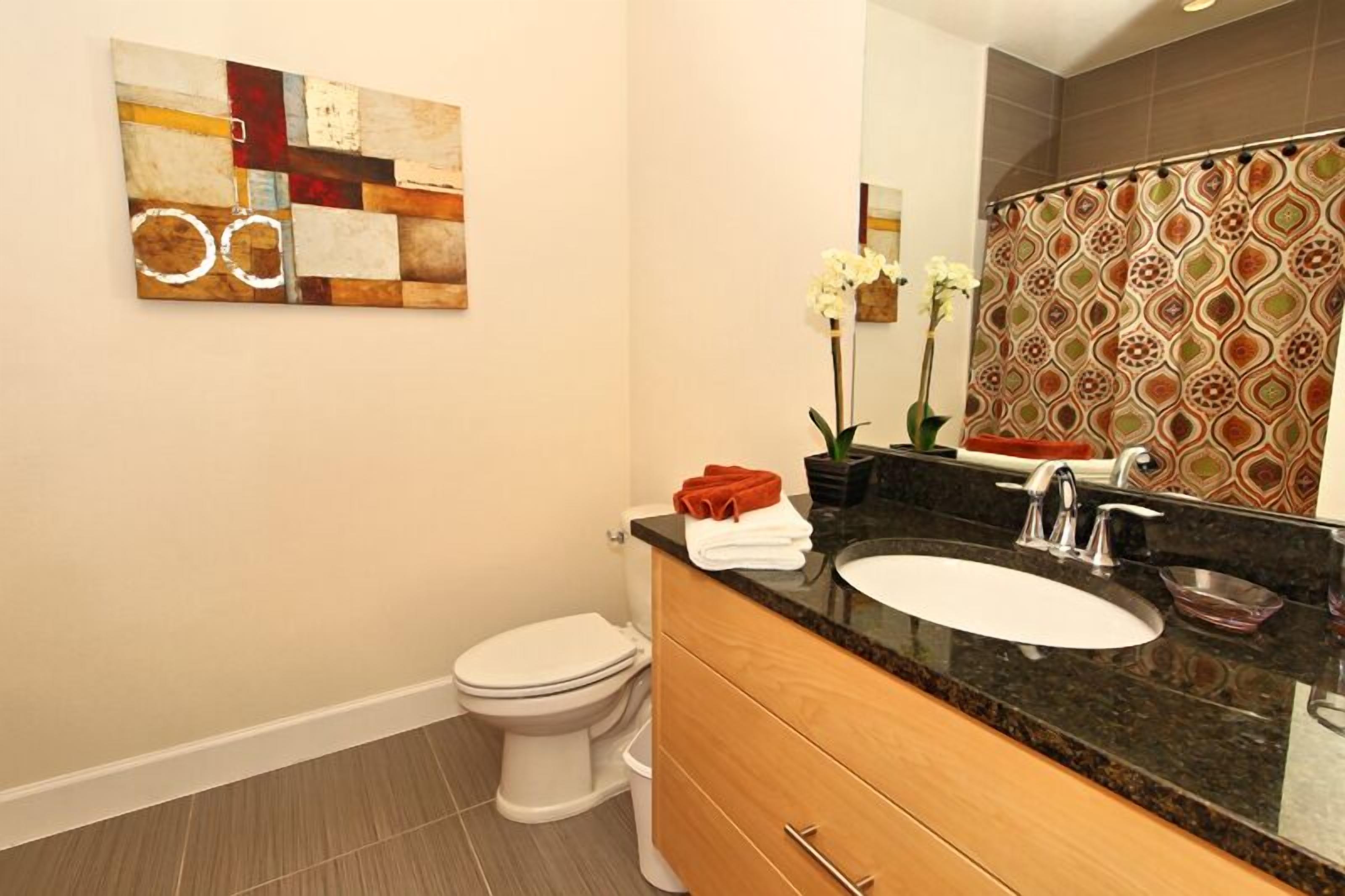 Un baño moderno con inodoro blanco, lavabo con espejo y cortina de ducha decorativa.