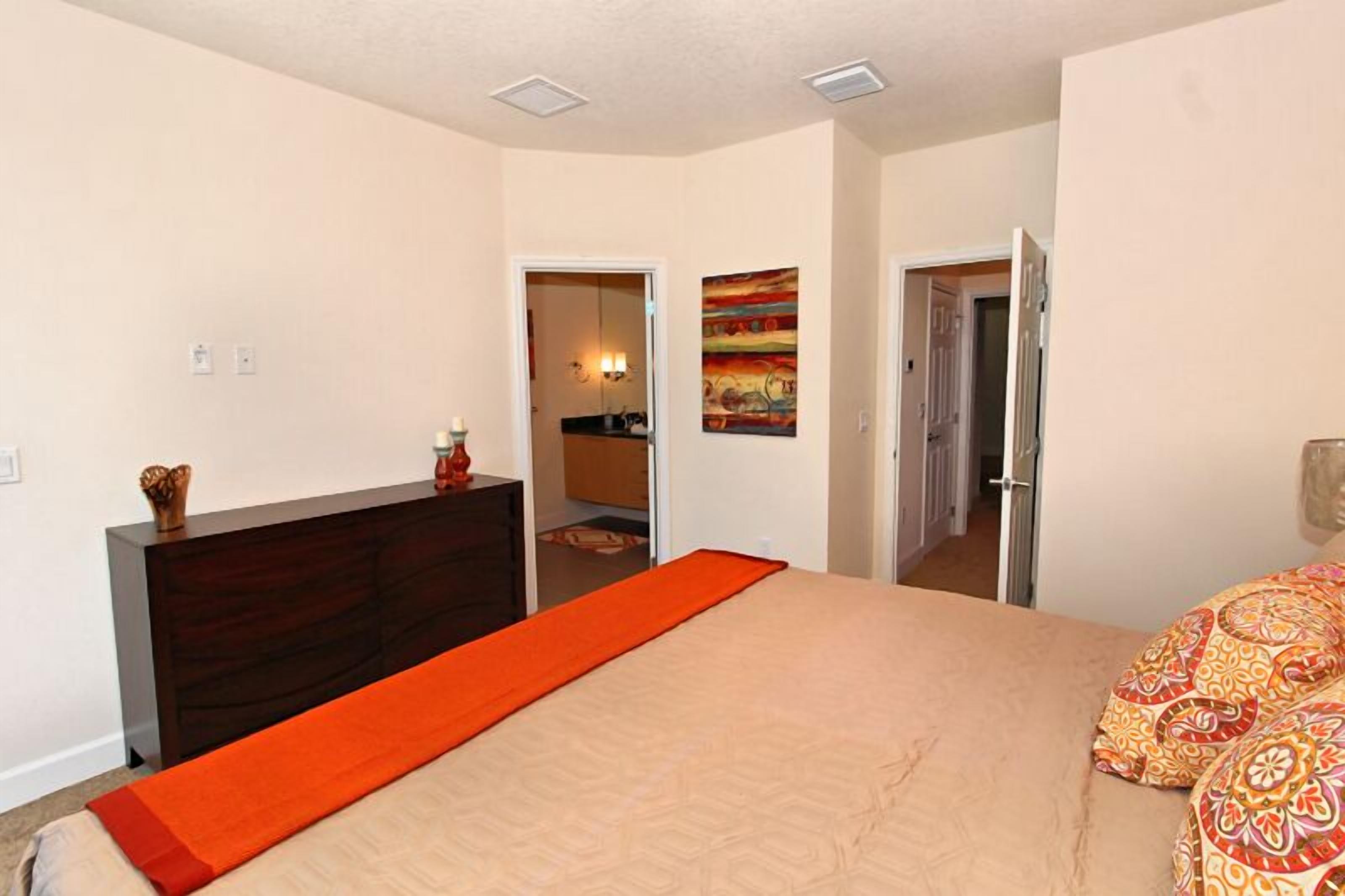 A bedroom with a bed, a dresser, and a door leading to a bathroom.