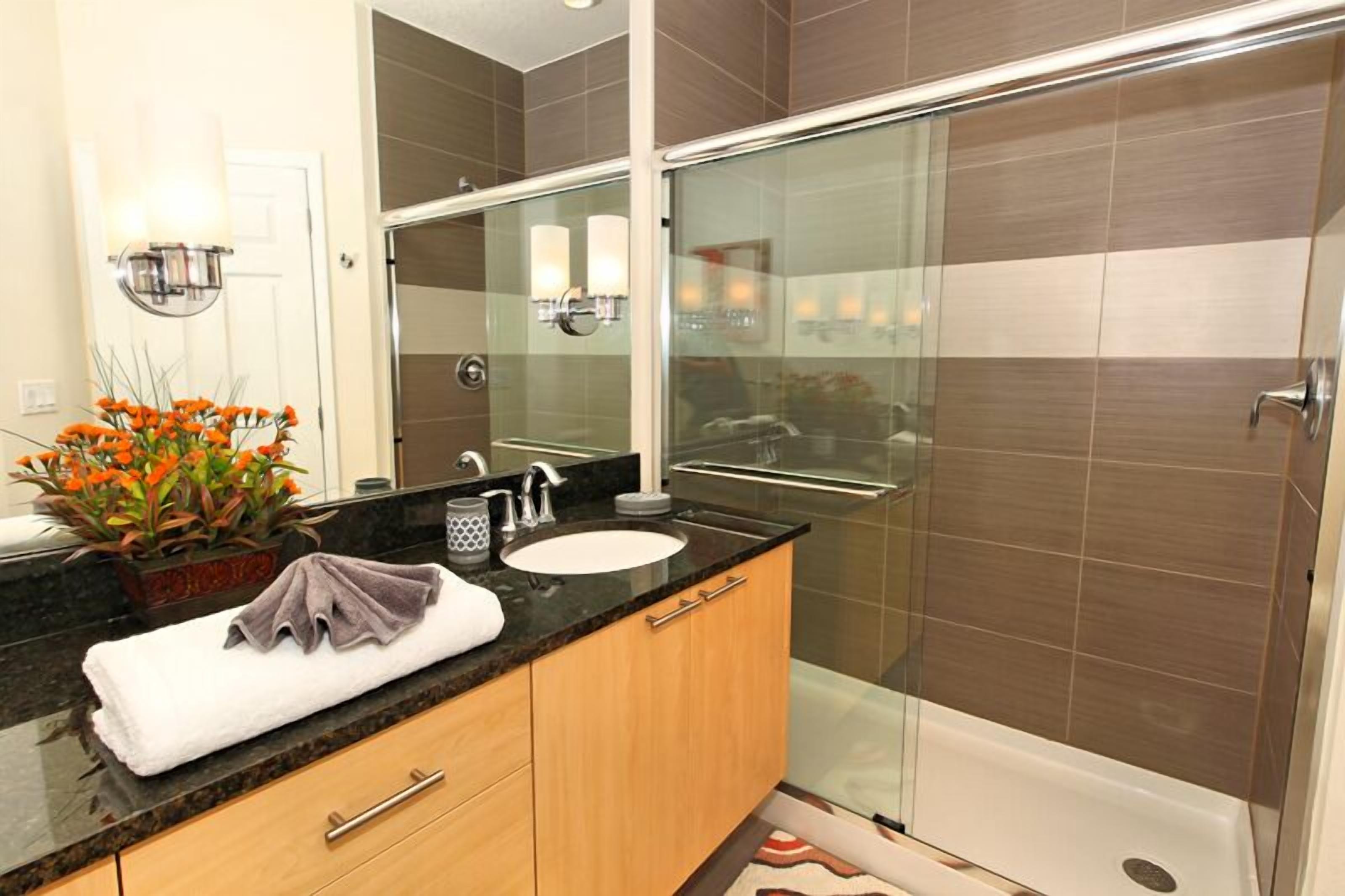 A modern bathroom with a glass-enclosed shower, a sink with a marble countertop, and a mirror above the sink.