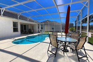 Un espace extérieur abrité comprenant une piscine, du mobilier de jardin et un parasol rouge.